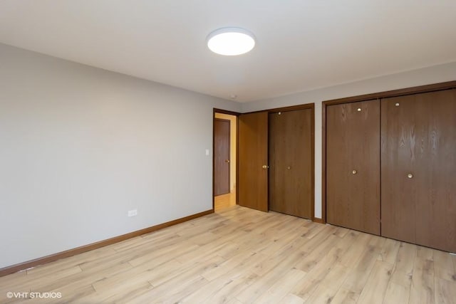 unfurnished bedroom featuring light wood-style floors, baseboards, and two closets