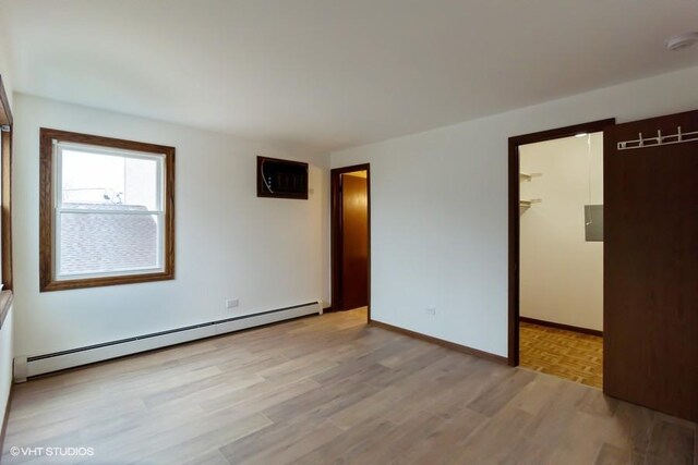 empty room featuring a baseboard heating unit, light wood finished floors, a wall unit AC, and baseboards