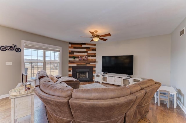 living room with baseboards, visible vents, ceiling fan, wood finished floors, and a fireplace