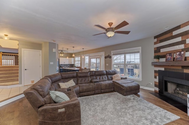 living area with a ceiling fan, a fireplace, stairway, and wood finished floors