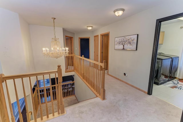 hallway featuring carpet, a chandelier, an upstairs landing, washer / dryer, and baseboards