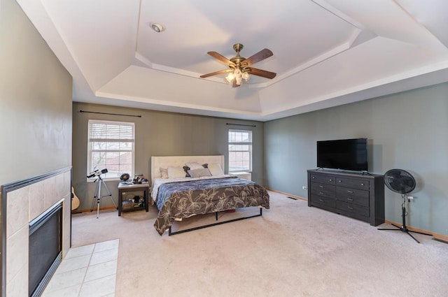 bedroom with carpet floors, a tray ceiling, multiple windows, and a tile fireplace