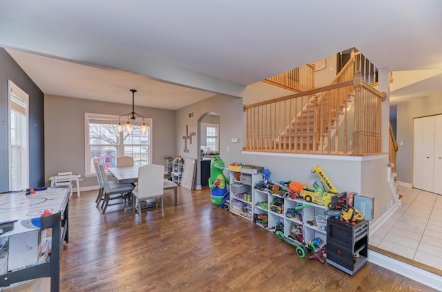 recreation room with arched walkways, a notable chandelier, baseboards, and wood finished floors