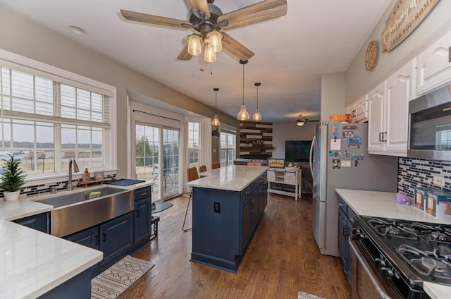 kitchen featuring gas range, a kitchen island, blue cabinetry, white cabinetry, and a sink