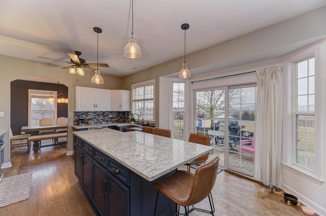 kitchen featuring arched walkways, decorative backsplash, white cabinets, a center island, and a sink