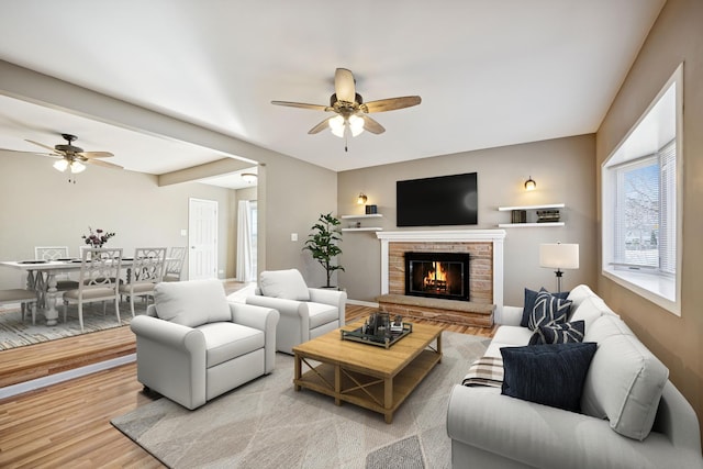 living room featuring a brick fireplace, a ceiling fan, and light wood finished floors