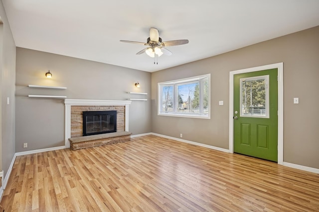 unfurnished living room featuring a glass covered fireplace, baseboards, light wood finished floors, and ceiling fan