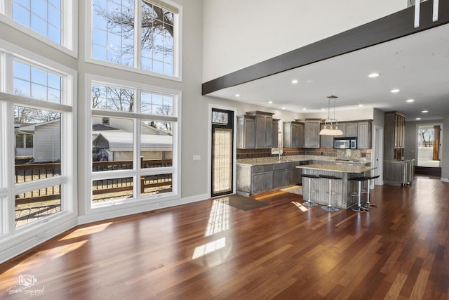 kitchen with dark wood-type flooring, a breakfast bar, stainless steel microwave, and a kitchen island