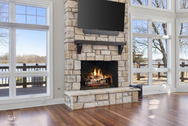 living room featuring baseboards, visible vents, wood finished floors, and a stone fireplace