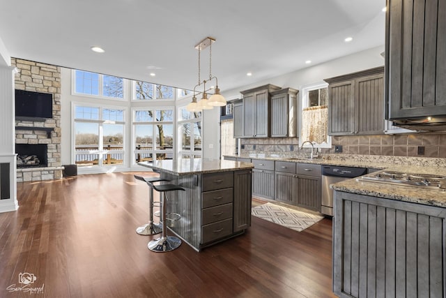 kitchen with dark wood-style floors, a center island, appliances with stainless steel finishes, open floor plan, and light stone countertops