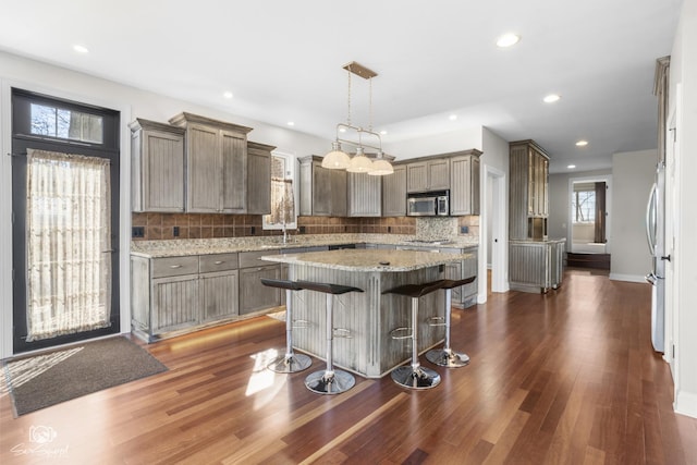 kitchen with dark wood-style floors, a center island, a breakfast bar area, gray cabinetry, and appliances with stainless steel finishes