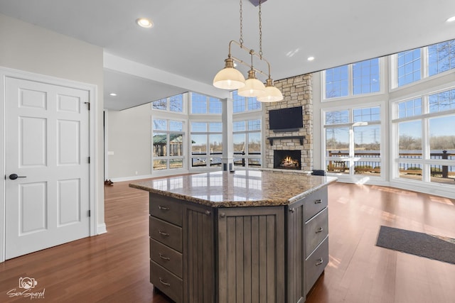 kitchen featuring a stone fireplace, dark brown cabinetry, dark wood-type flooring, open floor plan, and pendant lighting