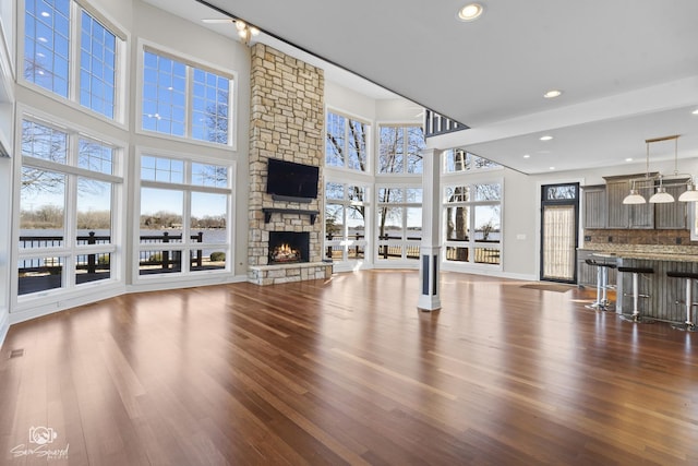 unfurnished living room with baseboards, a stone fireplace, wood finished floors, and ornate columns