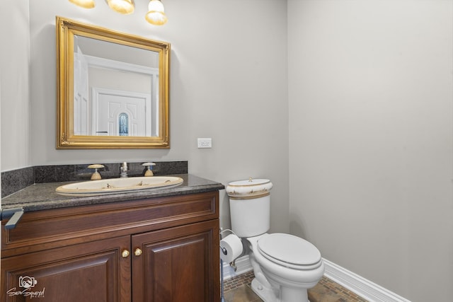 half bath with baseboards, vanity, and toilet