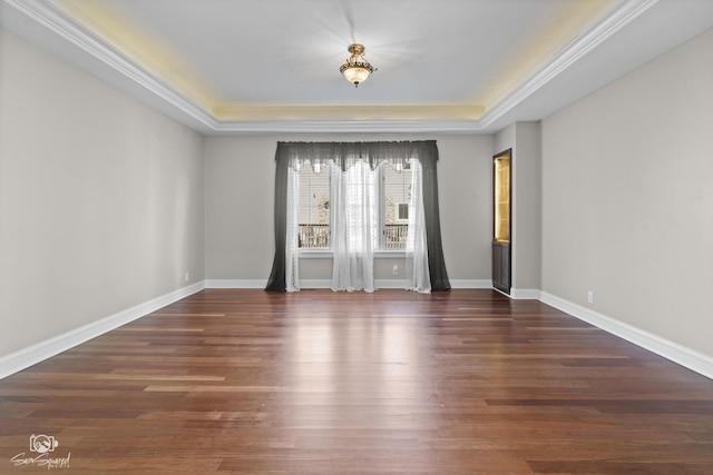 empty room featuring baseboards, crown molding, a tray ceiling, and wood finished floors