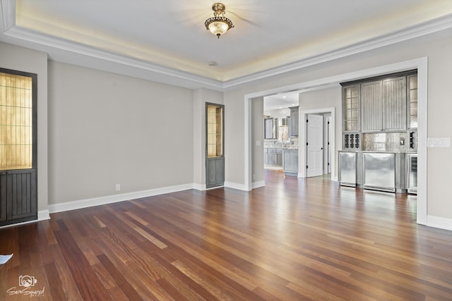 unfurnished living room featuring dark wood-style flooring, a raised ceiling, beverage cooler, and baseboards