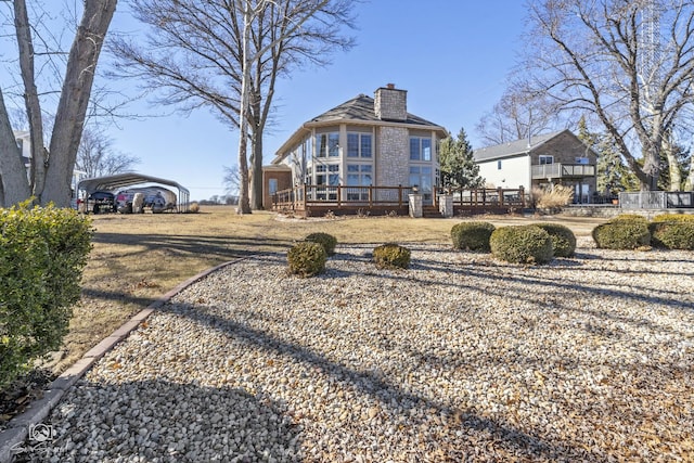 rear view of property featuring a chimney, a wooden deck, and a detached carport