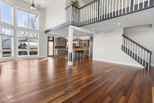 unfurnished living room with dark wood-type flooring, visible vents, ceiling fan, and stairs