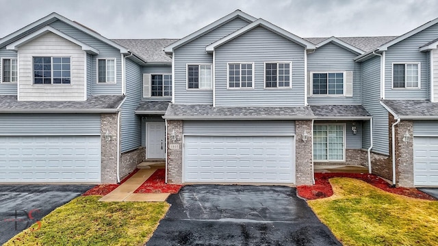 multi unit property with a garage, aphalt driveway, a shingled roof, and brick siding