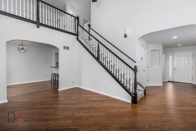 stairway featuring arched walkways, wood finished floors, a towering ceiling, visible vents, and baseboards