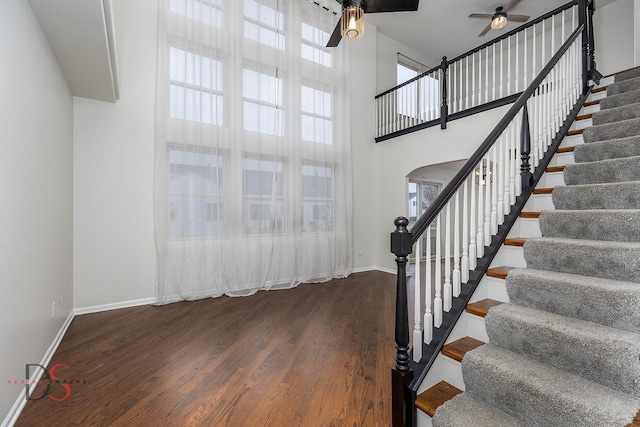 stairway with arched walkways, a high ceiling, ceiling fan, wood finished floors, and baseboards