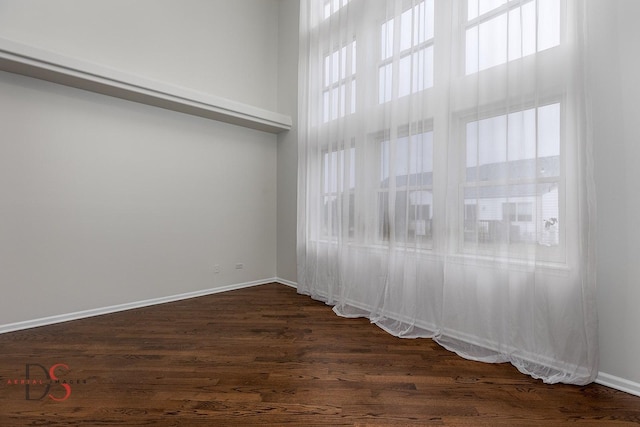 unfurnished room featuring a towering ceiling, baseboards, and dark wood-type flooring