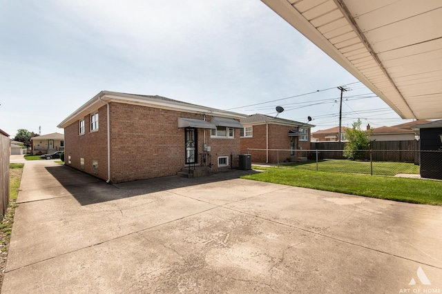 back of house with brick siding, fence, entry steps, central AC unit, and a lawn