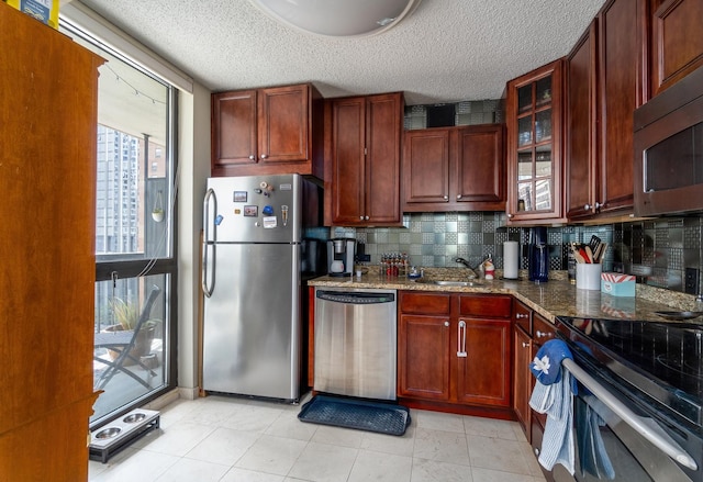 kitchen with glass insert cabinets, decorative backsplash, stone counters, appliances with stainless steel finishes, and a sink