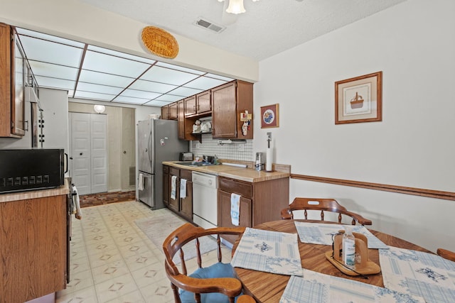 kitchen with visible vents, black microwave, light countertops, freestanding refrigerator, and white dishwasher