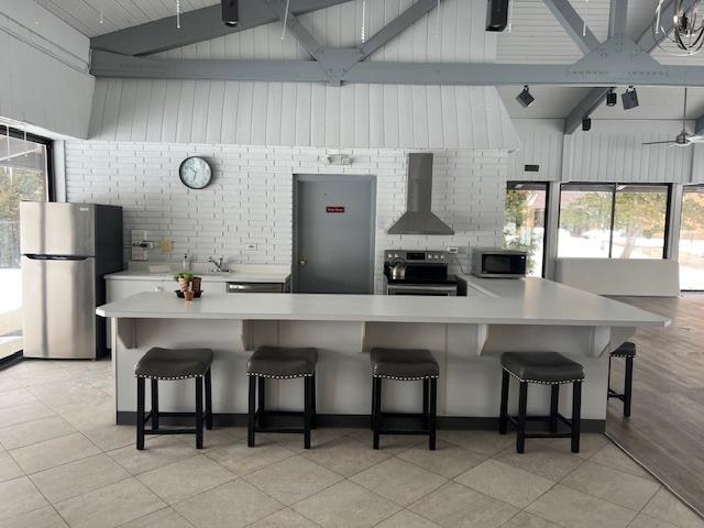 kitchen featuring a kitchen bar, appliances with stainless steel finishes, wall chimney exhaust hood, and light countertops