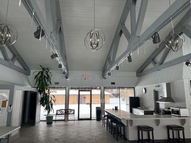 kitchen with stainless steel microwave, lofted ceiling, an inviting chandelier, and wall chimney exhaust hood