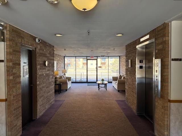 corridor with floor to ceiling windows, elevator, carpet, and brick wall