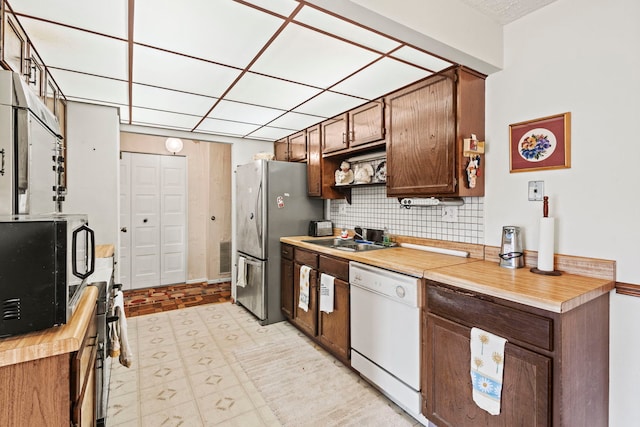 kitchen featuring light floors, open shelves, a sink, decorative backsplash, and appliances with stainless steel finishes