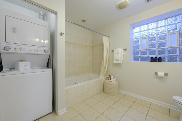 bathroom with baseboards, tile patterned flooring, stacked washer / drying machine, toilet, and tiled shower / bath