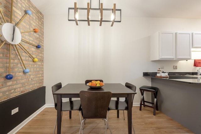 dining room featuring baseboards, brick wall, and light wood finished floors