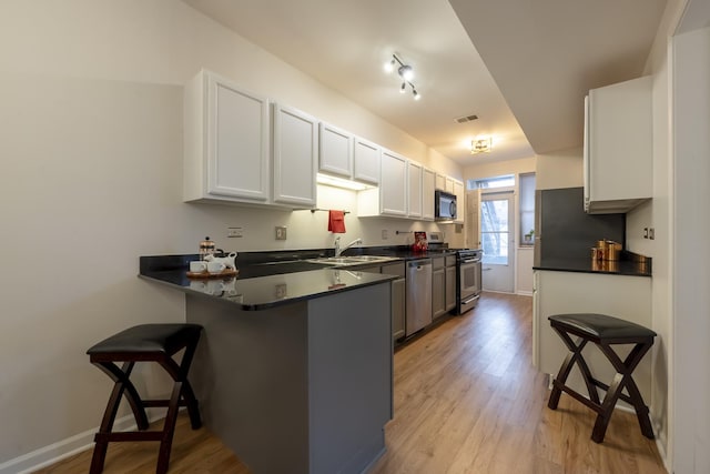 kitchen with a breakfast bar, light wood-style flooring, dark countertops, appliances with stainless steel finishes, and a peninsula