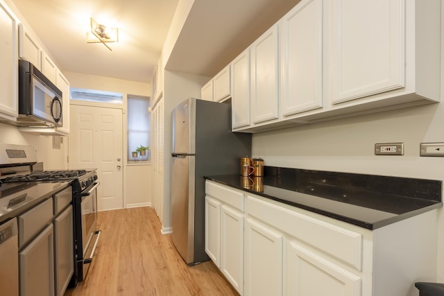 kitchen with dark countertops, light wood-style flooring, white cabinets, and stainless steel appliances