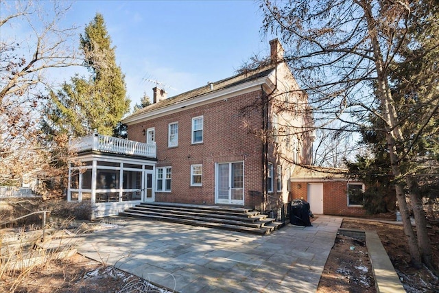 rear view of property with a patio, brick siding, a chimney, and a sunroom