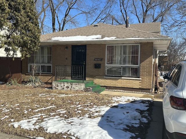 bungalow-style house with a shingled roof, brick siding, and fence