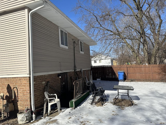 snow covered property with brick siding and fence