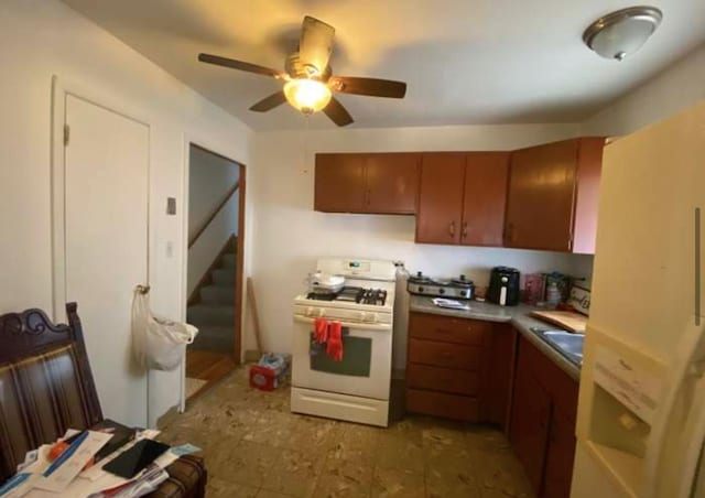 kitchen with ceiling fan, light countertops, white gas range, and brown cabinets