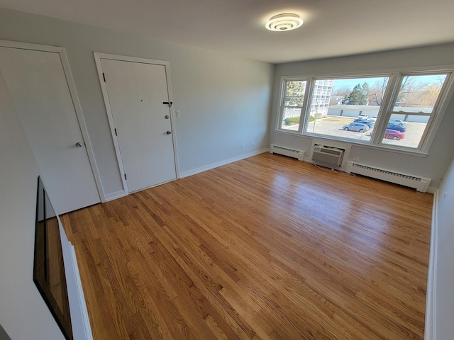 spare room with a baseboard heating unit, an AC wall unit, baseboards, and light wood finished floors