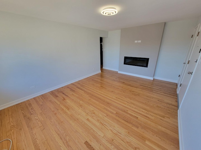 unfurnished living room with light wood-style flooring, baseboards, and a glass covered fireplace