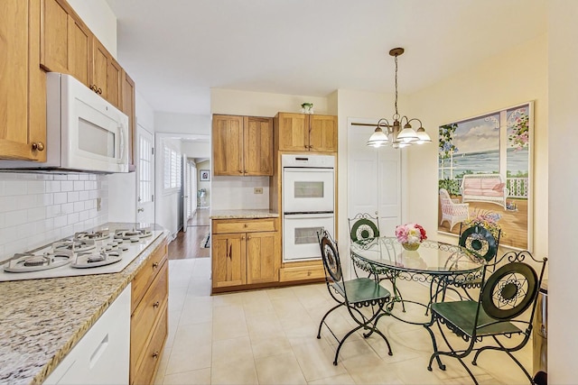 kitchen with white appliances, an inviting chandelier, pendant lighting, brown cabinets, and backsplash