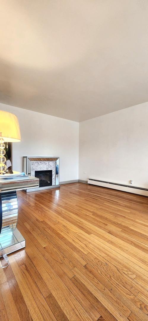 unfurnished living room with a baseboard heating unit, wood finished floors, and a premium fireplace