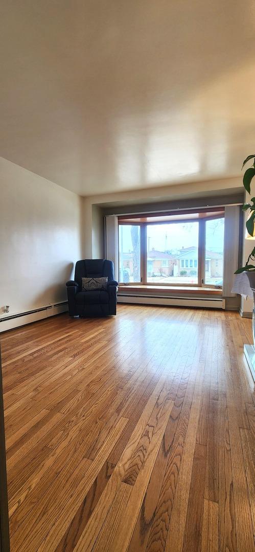 unfurnished living room featuring plenty of natural light, baseboard heating, and hardwood / wood-style floors