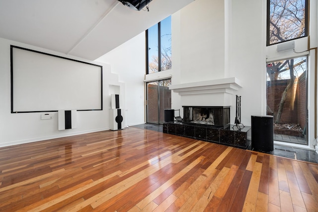 cinema room featuring a tiled fireplace, a high ceiling, baseboards, and hardwood / wood-style floors