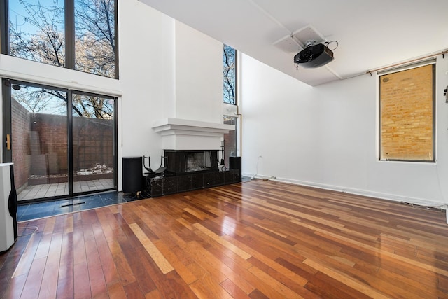 unfurnished living room featuring a tiled fireplace, a high ceiling, baseboards, and wood-type flooring