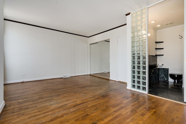 empty room featuring visible vents, wood finished floors, baseboards, and ornamental molding