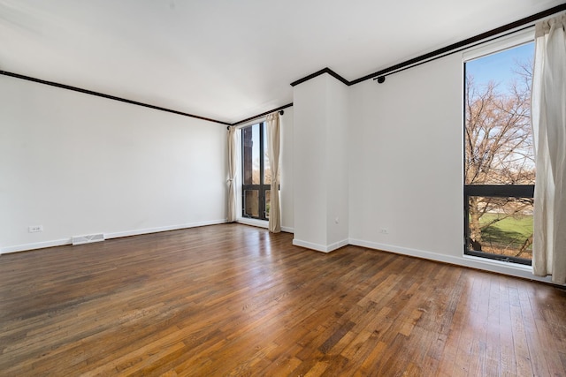 unfurnished room with visible vents, baseboards, crown molding, and dark wood-type flooring